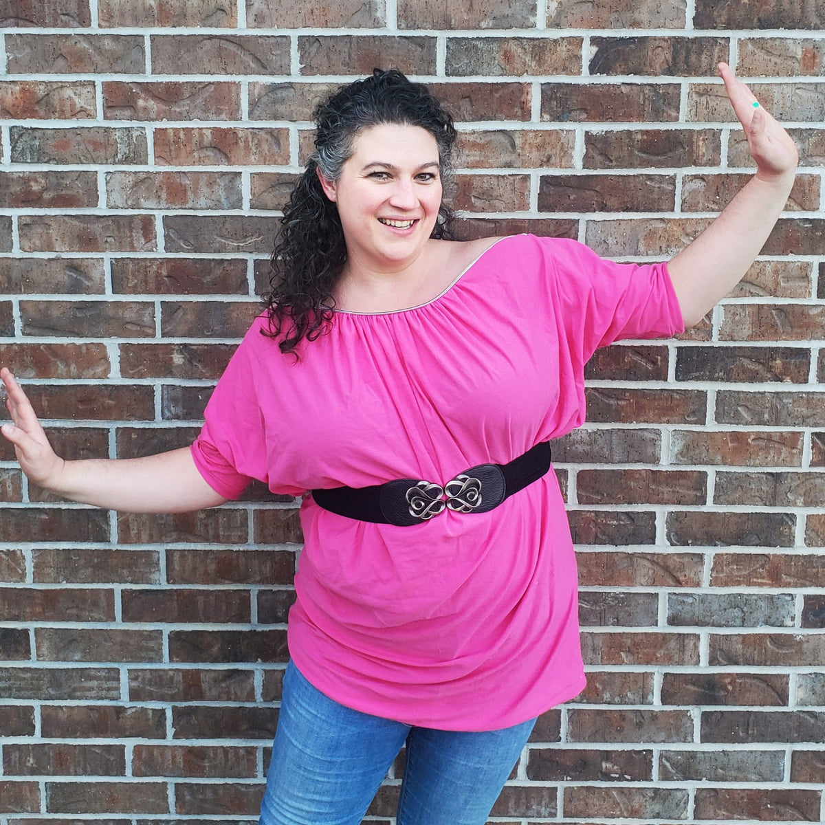 Woman in the pink boatneck zipper shirt posing against a brick wall