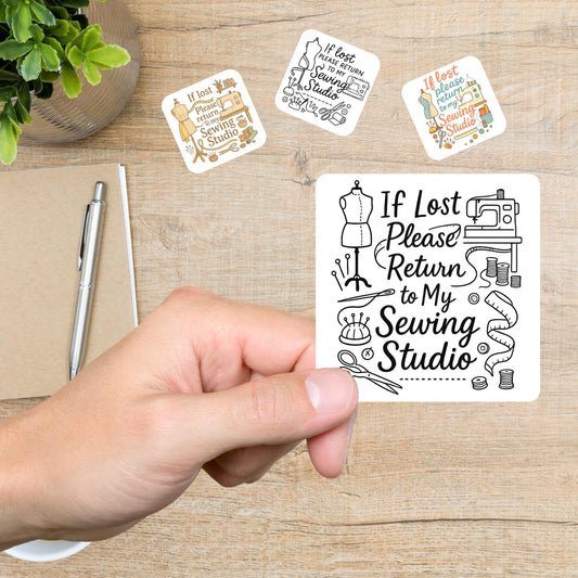 Hand holding an If Lost Please Return to My Sewing Studio sticker with three more sewing stickers on a desk