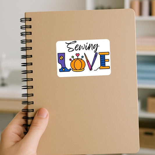 Sewing Love sticker in color on a kraft notebook, with LOVE spelled using a presser foot, pincushion, needle and spool