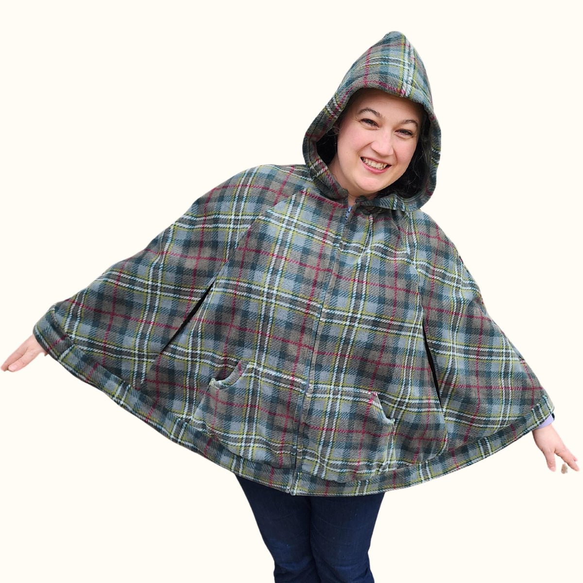 Smiling woman in a green plaid hoodie capelet with arms spread out
