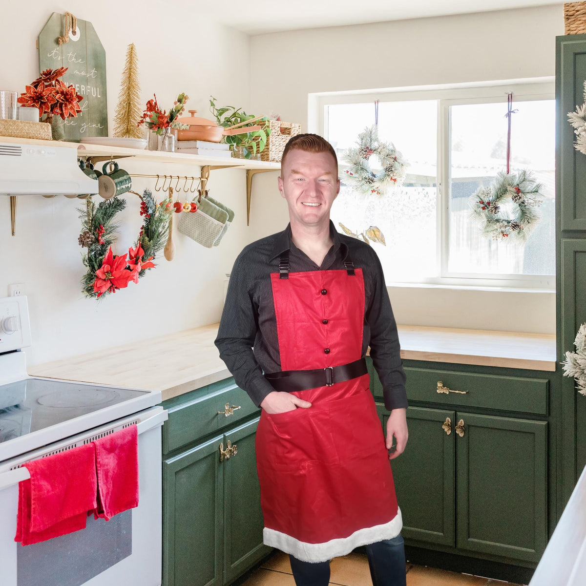 Man wearing a red Santa apron with black belt and white trim in a Christmas kitchen