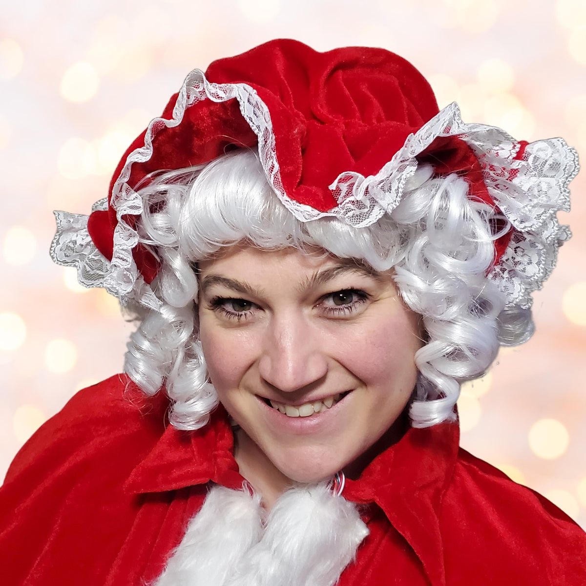 Woman in a white curly wig wearing a red velvet Mrs Claus mop cap with lace trim