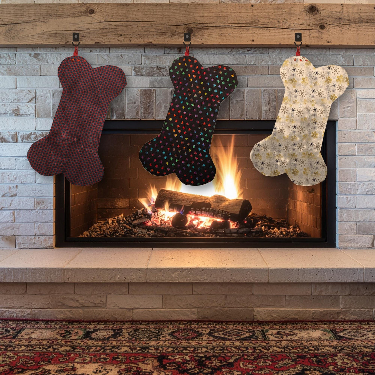 Three dog bone stockings in burgundy plaid, rainbow paw print and gold snowflake fabrics hanging over a fireplace