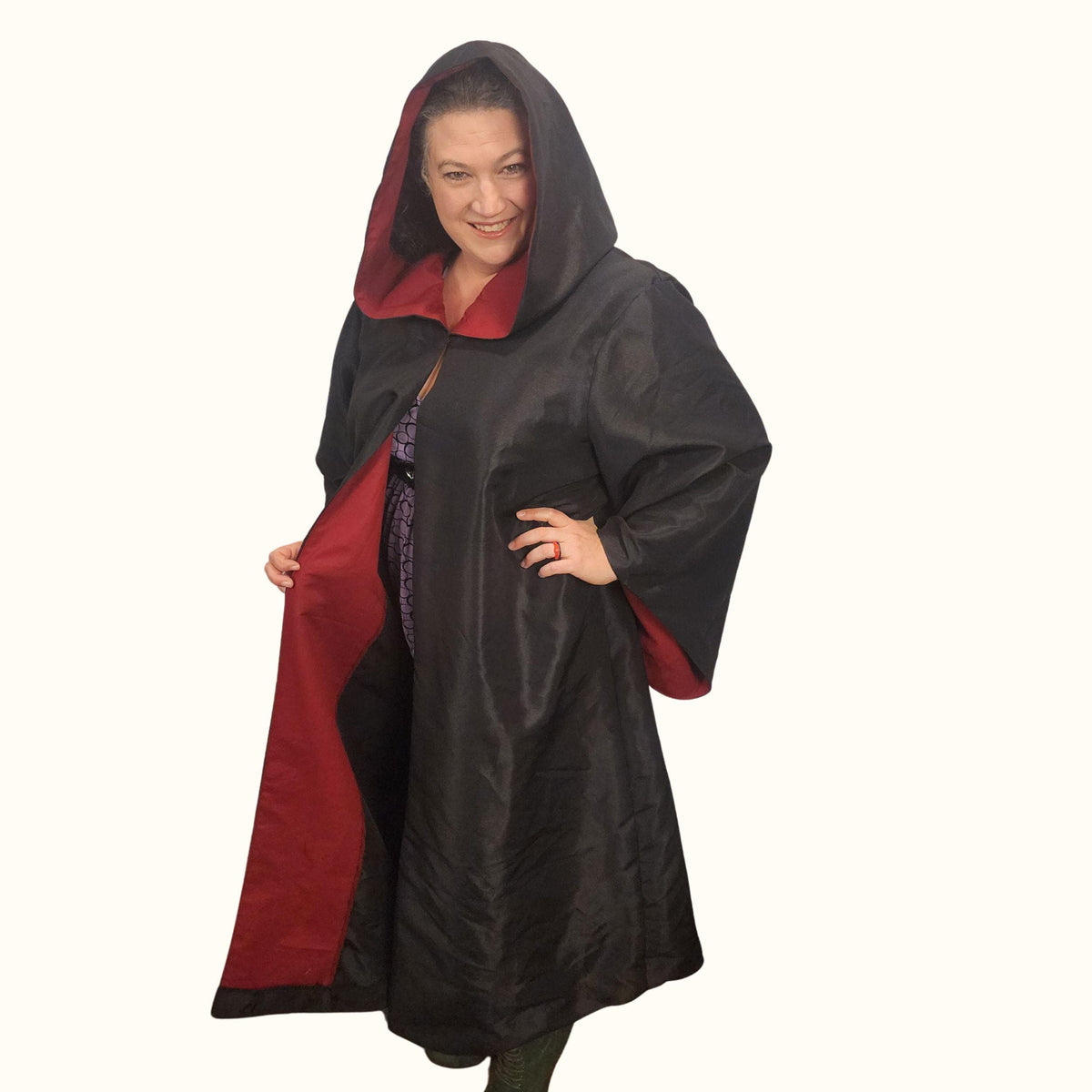 Woman wearing the hooded wizard robe with the hood up, holding it open to show the red facing and long flowing black body