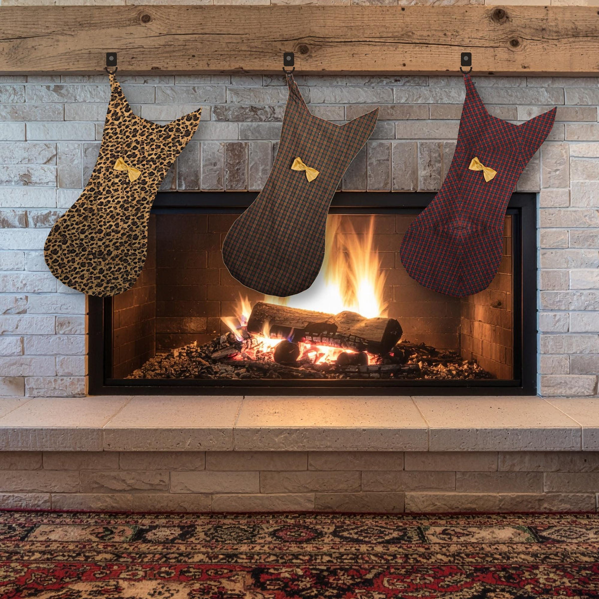 Three cat stockings in leopard print, brown plaid and burgundy plaid with gold bows hanging on a fireplace mantel
