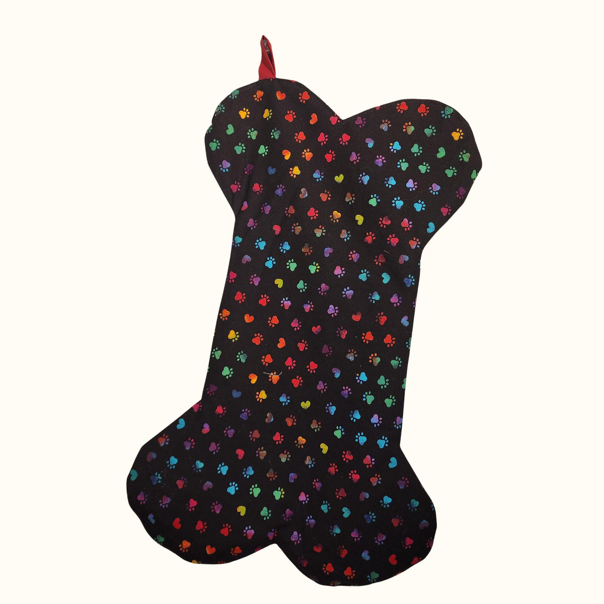 Finished dog bone shaped Christmas stocking in black fabric with rainbow paw prints and a red hanging loop