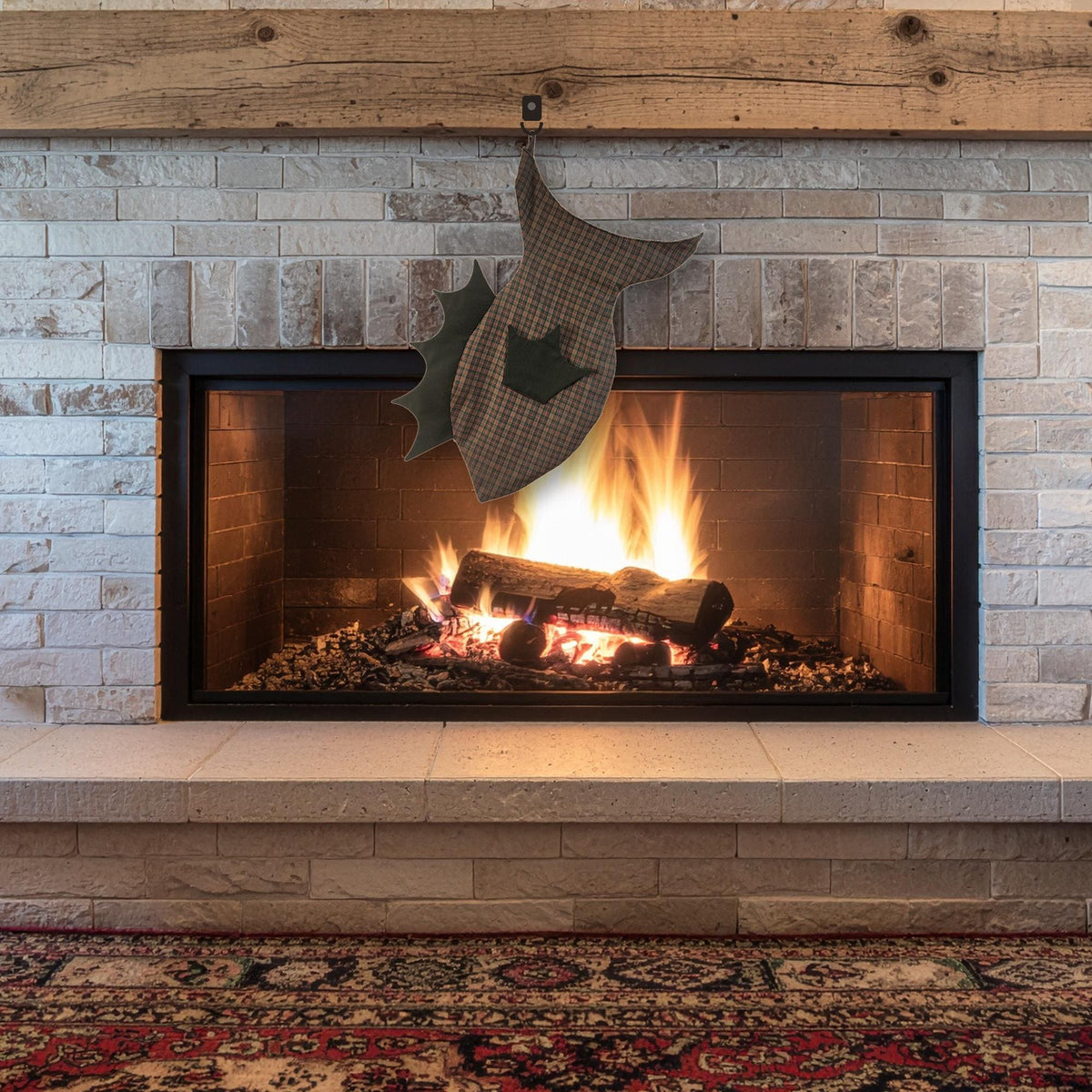 Brown plaid fish stocking with black fins hanging tail up over a lit fireplace